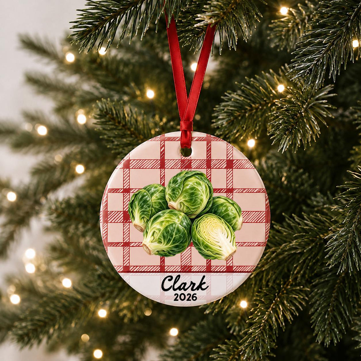 Personalized brussels sprouts ceramic ornament with name and year on red plaid hanging on a lit Christmas tree