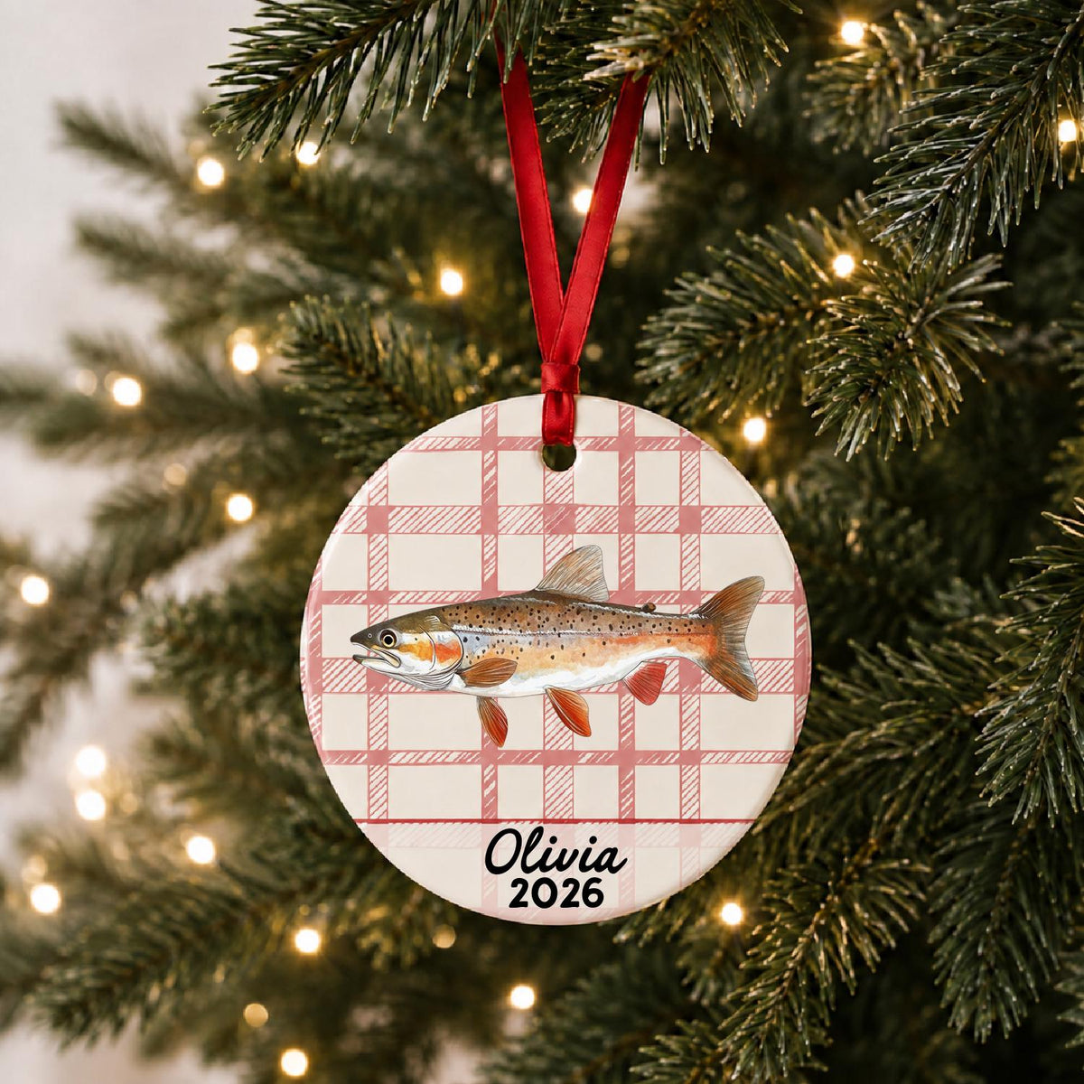 Personalized rainbow trout ceramic ornament with name and year on red plaid hanging on a lit Christmas tree