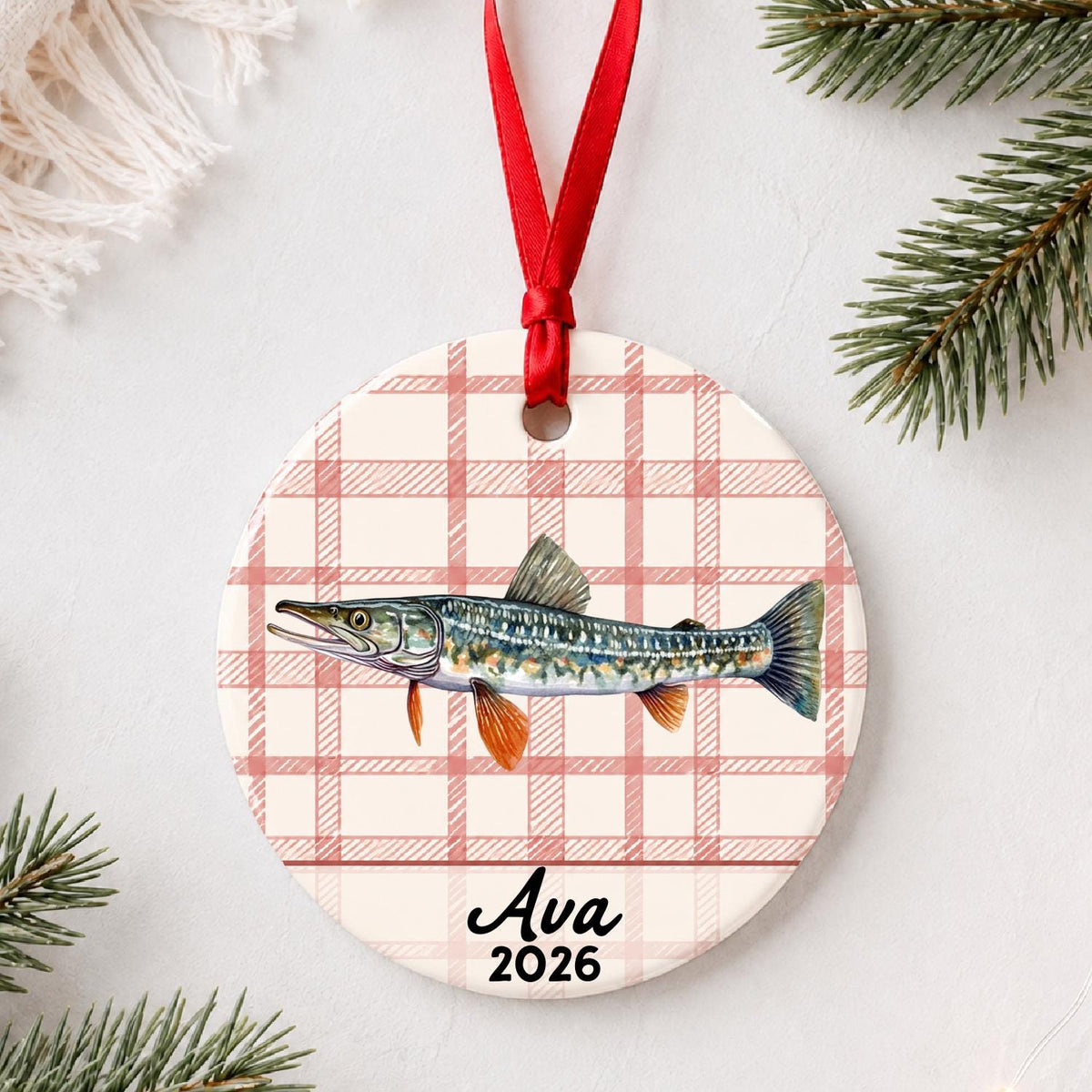 Personalized northern pike ceramic ornament with name and year on red plaid styled with pine branches on a soft white background