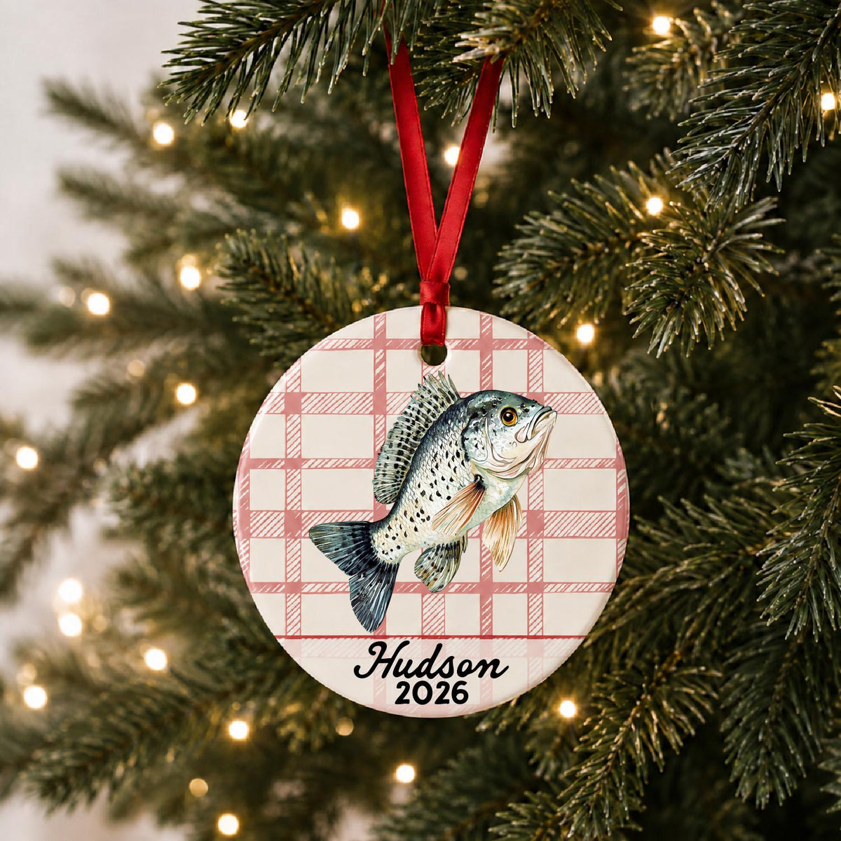 Personalized crappie ceramic ornament with name and year on red plaid hanging on a lit Christmas tree