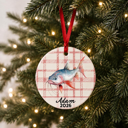 Personalized red-finned catfish ceramic ornament with name and year on red plaid hanging on a lit Christmas tree