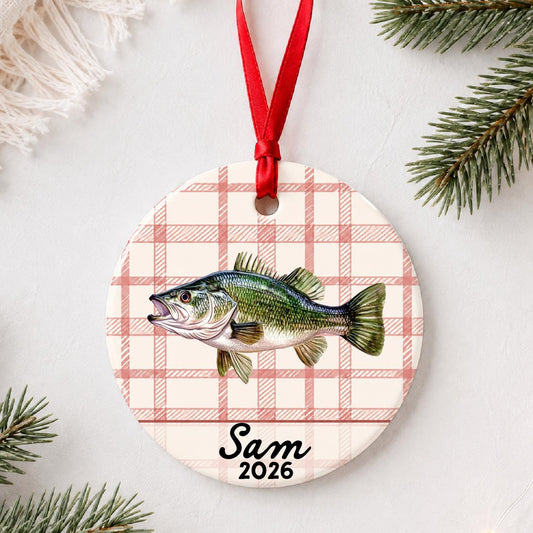 Personalized largemouth bass ceramic ornament with name and year on red plaid styled with pine branches on a soft white background