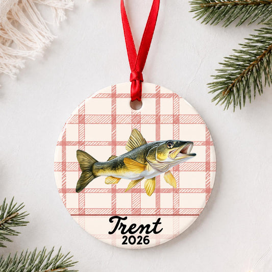 Personalized golden walleye ceramic ornament with name and year on red plaid styled with pine branches on a soft white background