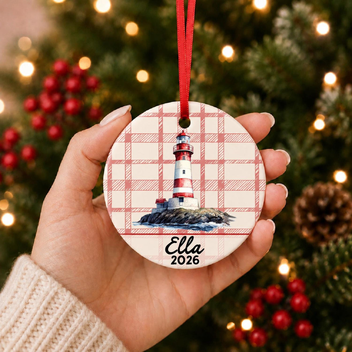 Hand holding the personalized island lighthouse ceramic ornament with name and year on red plaid in front of a Christmas tree