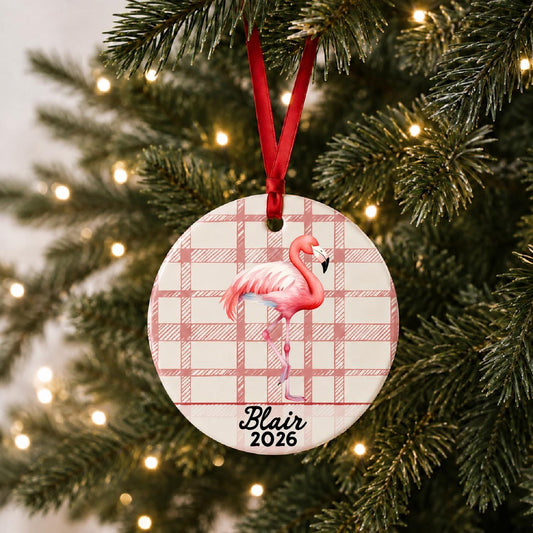 Personalized flamingo ceramic ornament with name and year on red plaid hanging on a lit Christmas tree
