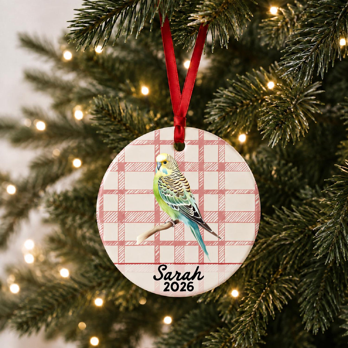 Personalized budgerigar ceramic ornament with name and year on red plaid hanging on a lit Christmas tree