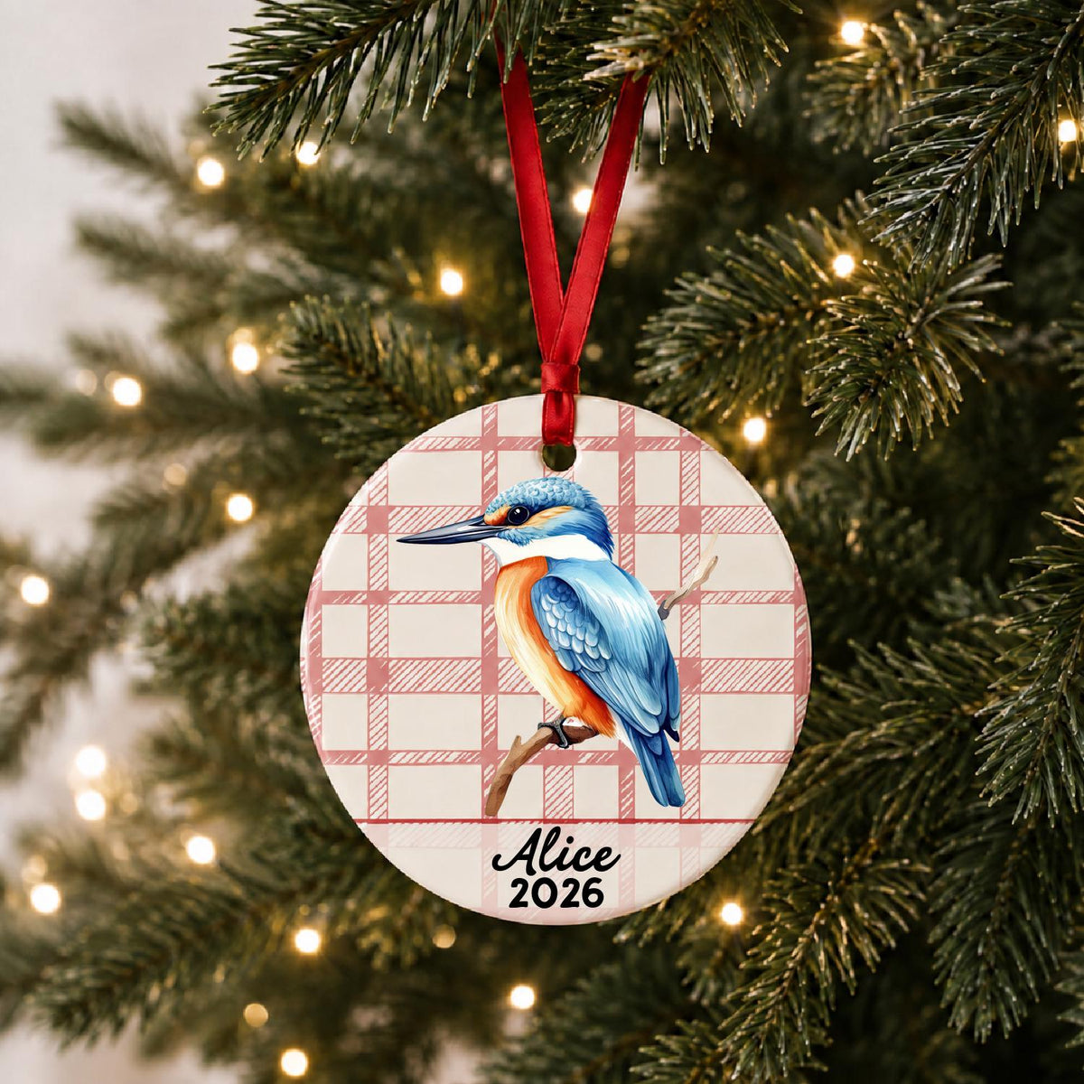 Personalized kingfisher ceramic ornament with name and year on red plaid hanging on a lit Christmas tree