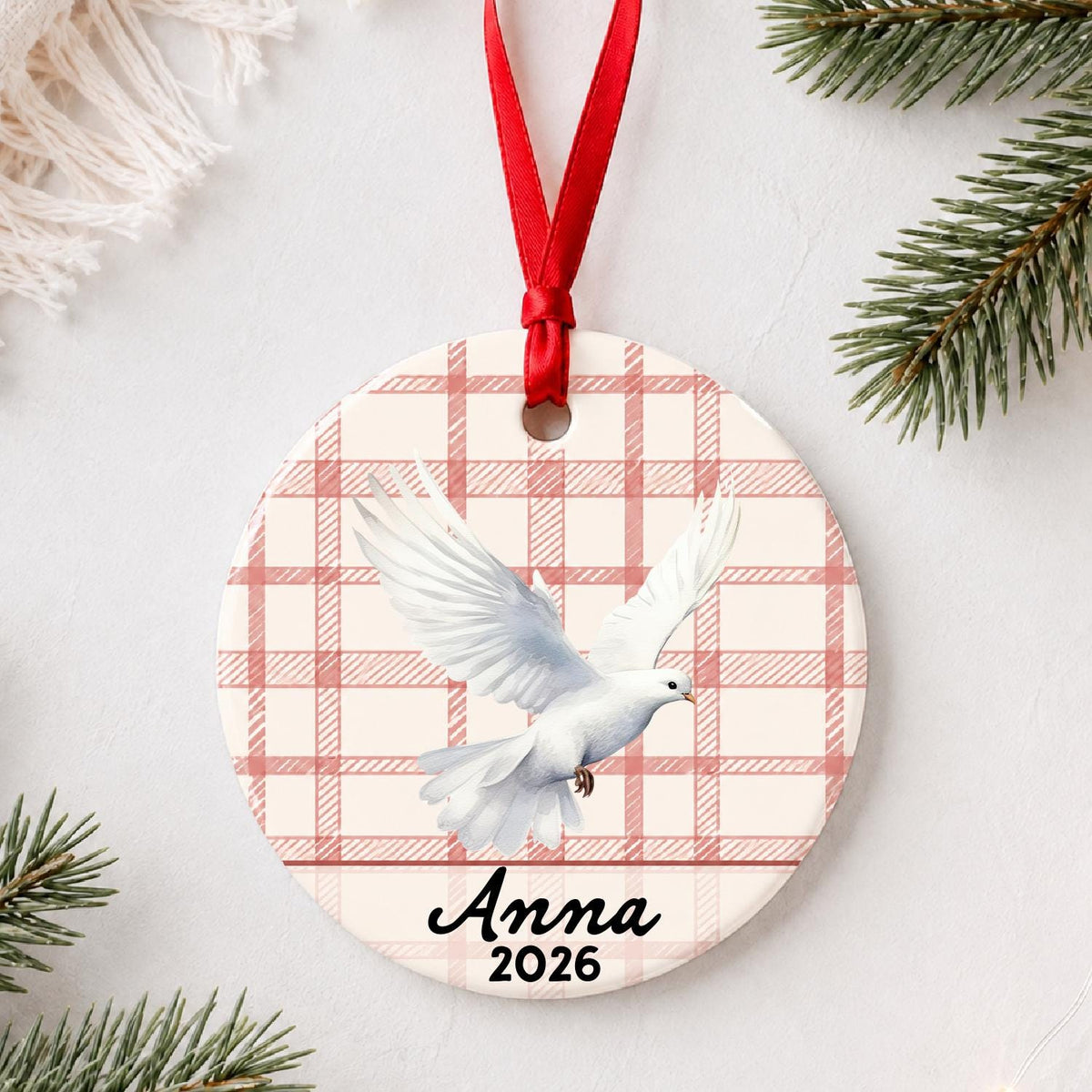 Personalized white dove ceramic ornament with name and year on red plaid styled with pine branches on a soft white background