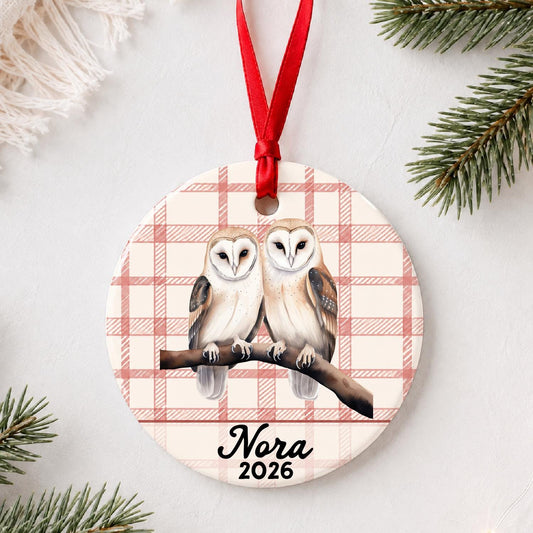 Personalized barn owl pair ceramic ornament with name and year on red plaid styled with pine branches on a soft white background