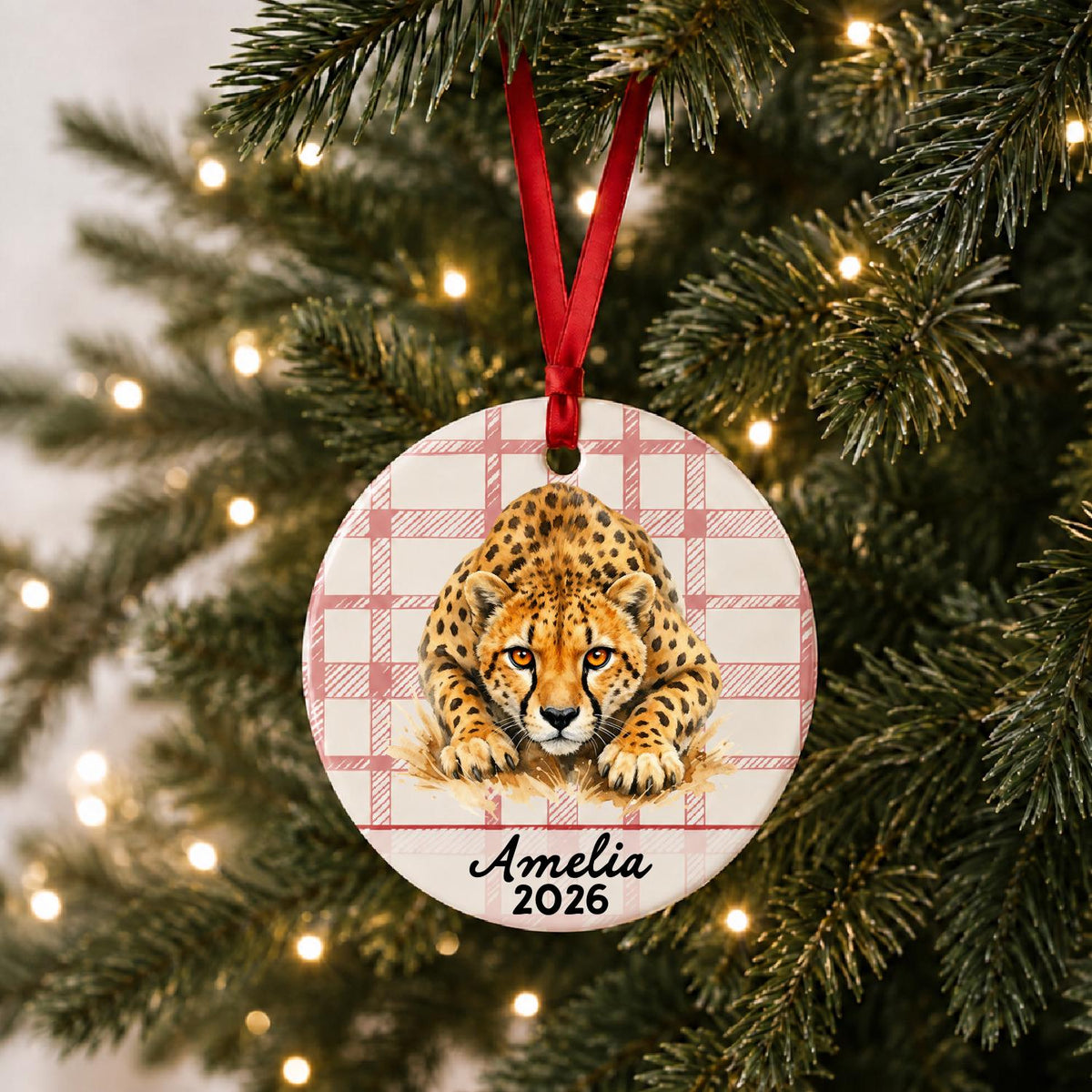 Personalized cheetah ceramic ornament with name and year on red plaid hanging on a lit Christmas tree