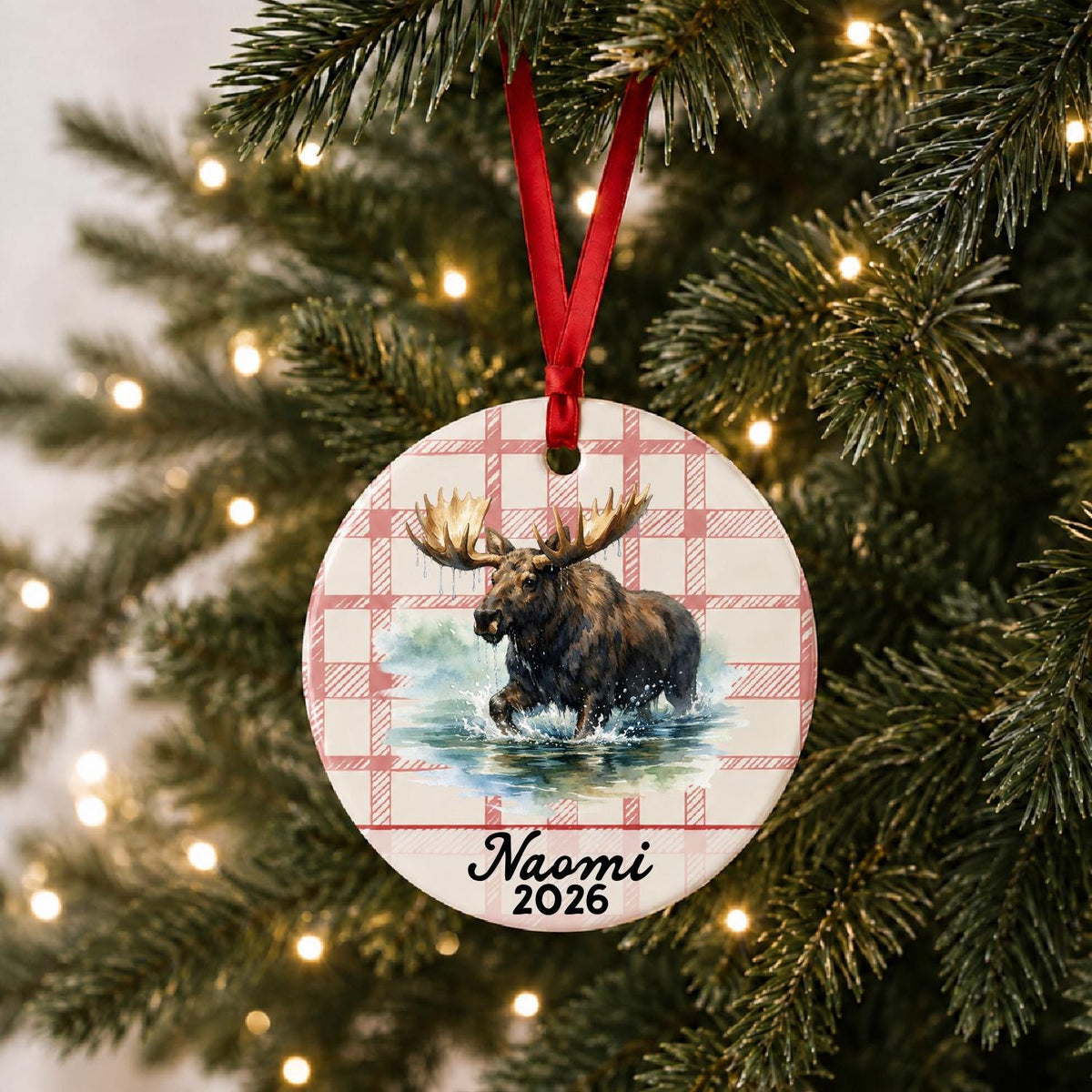 Personalized bull moose ceramic ornament with name and year on red plaid hanging on a lit Christmas tree