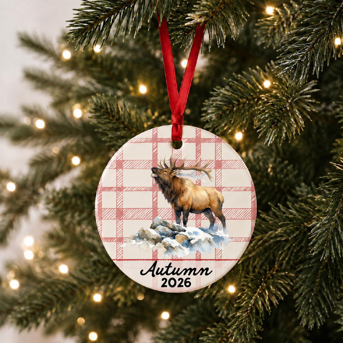 Personalized bull elk ceramic ornament with name and year on red plaid hanging on a lit Christmas tree