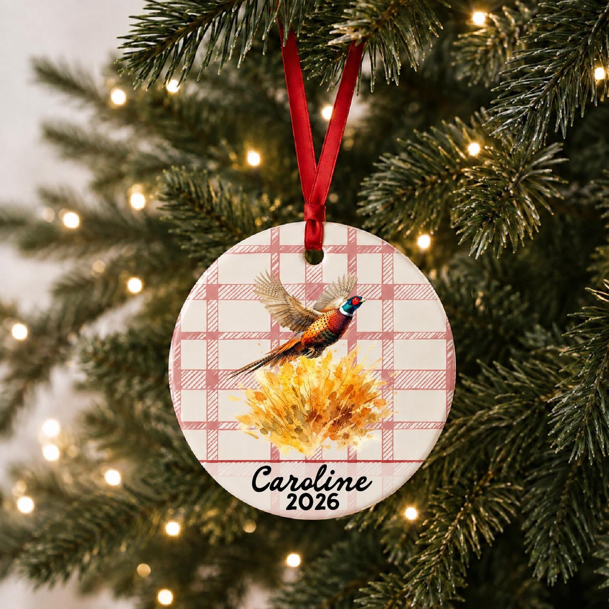 Personalized ring-necked pheasant ceramic ornament with name and year on red plaid hanging on a lit Christmas tree