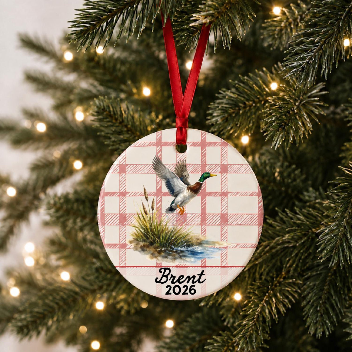 Personalized mallard duck ceramic ornament with name and year on red plaid hanging on a lit Christmas tree