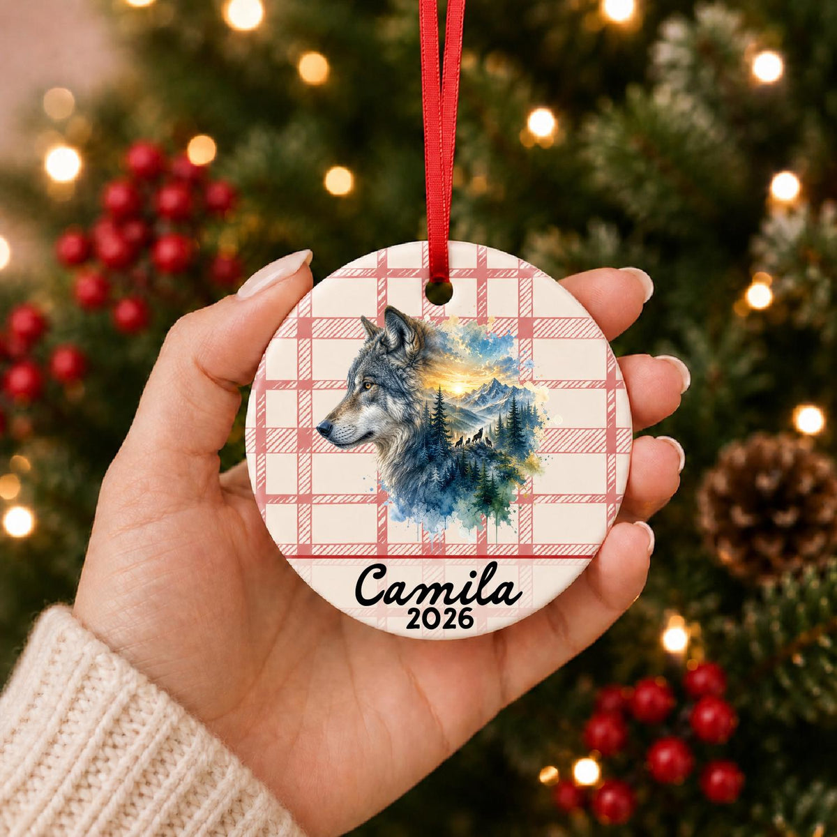 Hand holding the personalized grey wolf ceramic ornament with name and year on red plaid in front of a Christmas tree