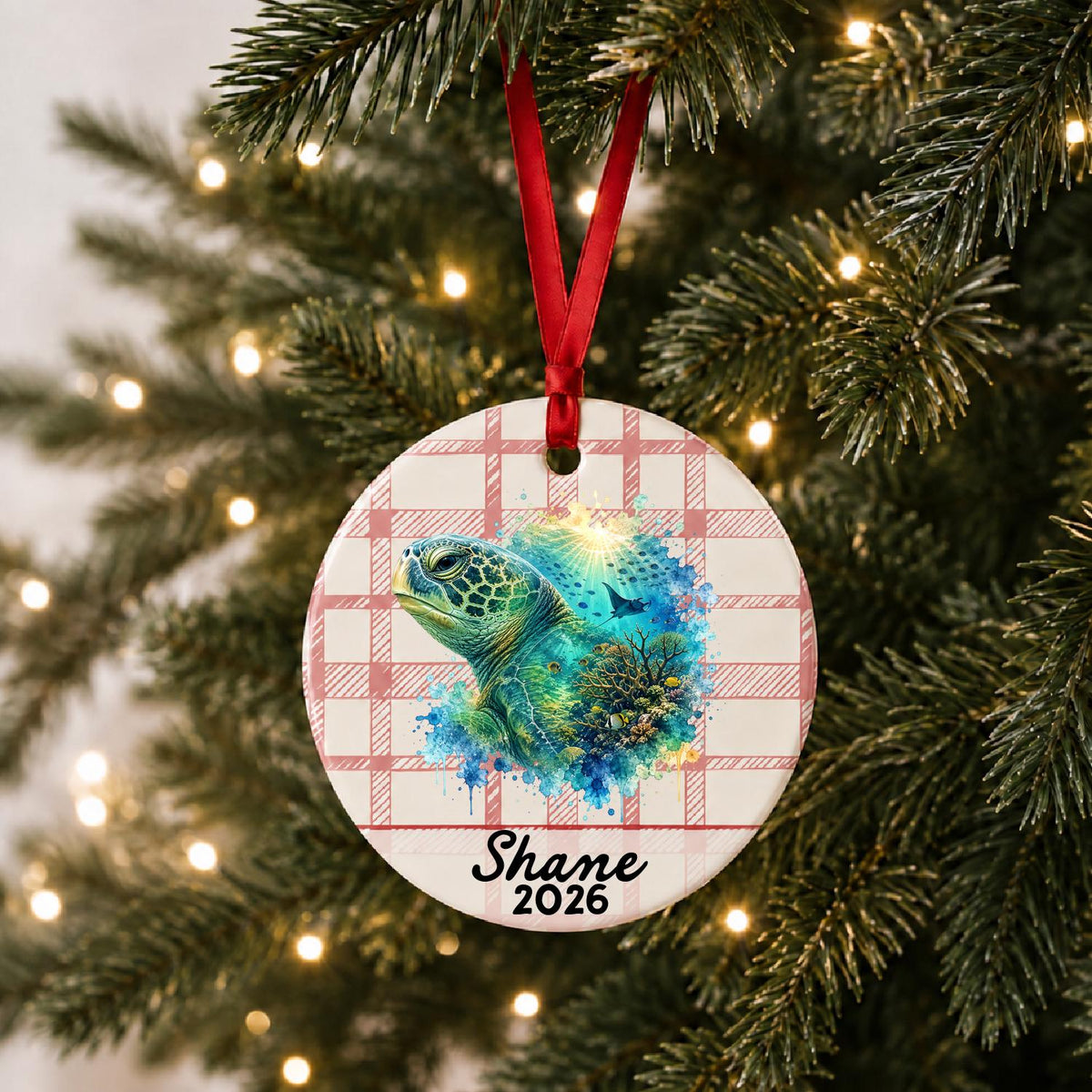 Personalized green sea turtle ceramic ornament with name and year on red plaid hanging on a lit Christmas tree
