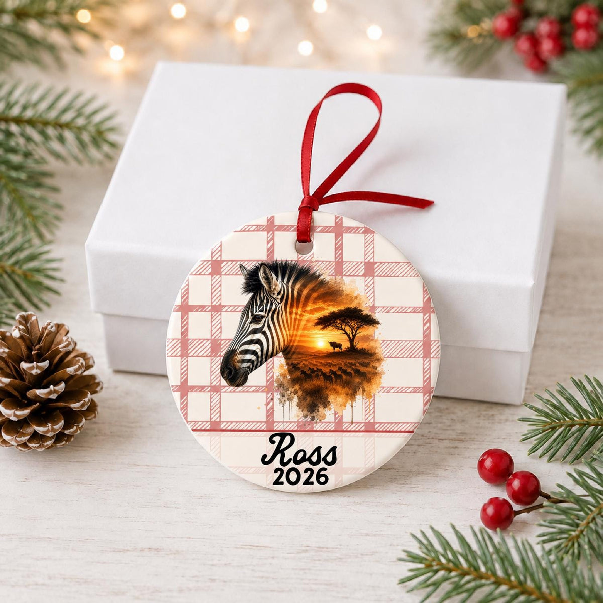 Personalized plains zebra ceramic ornament with name and year on red plaid in front of a white gift box with pinecones and red berries