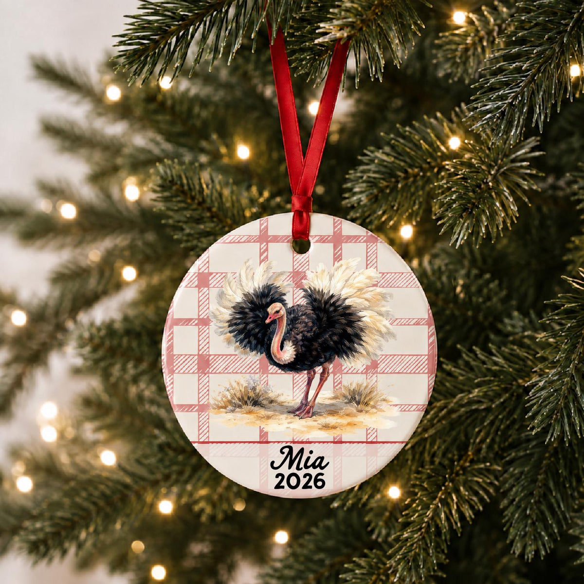 Personalized ostrich ceramic ornament with name and year on red plaid hanging on a lit Christmas tree