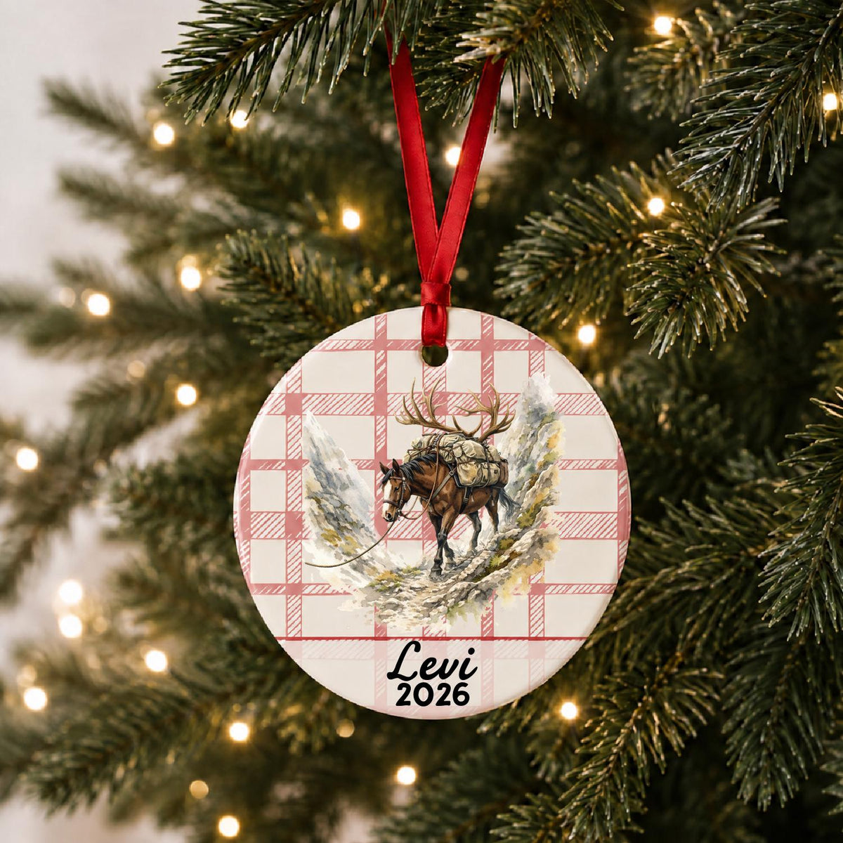 Personalized pack horse ceramic ornament with name and year on red plaid hanging on a lit Christmas tree