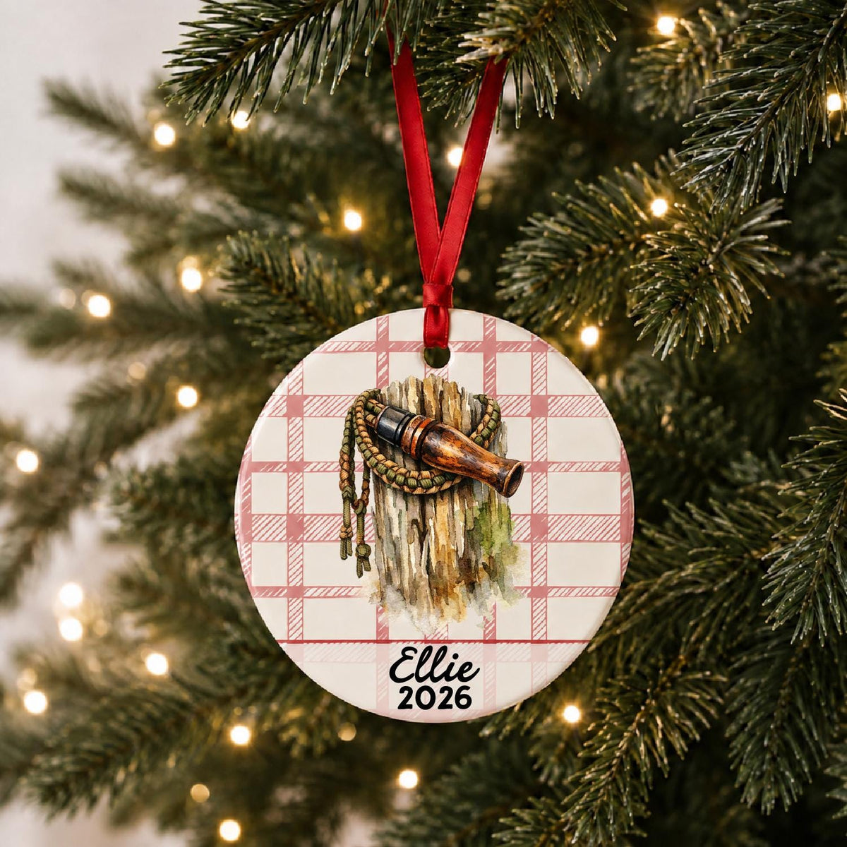 Personalized duck call ceramic ornament with name and year on red plaid hanging on a lit Christmas tree