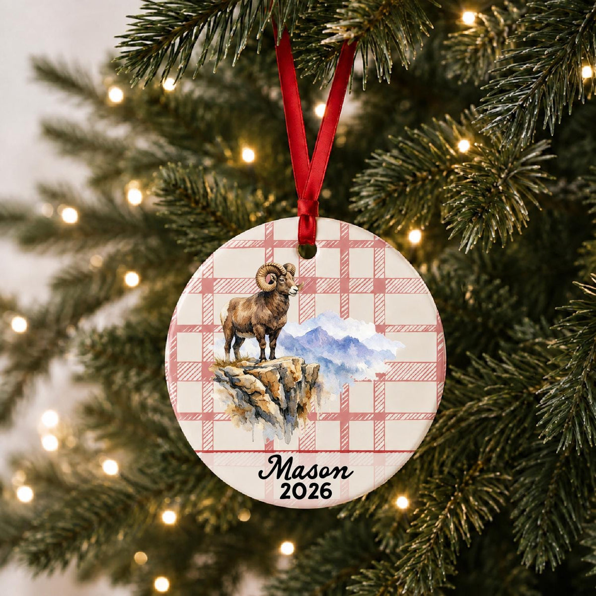 Personalized bighorn sheep ceramic ornament with name and year on red plaid hanging on a lit Christmas tree