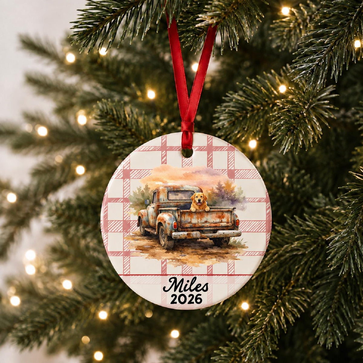 Personalized vintage truck and dog ceramic ornament with name and year on red plaid hanging on a lit Christmas tree