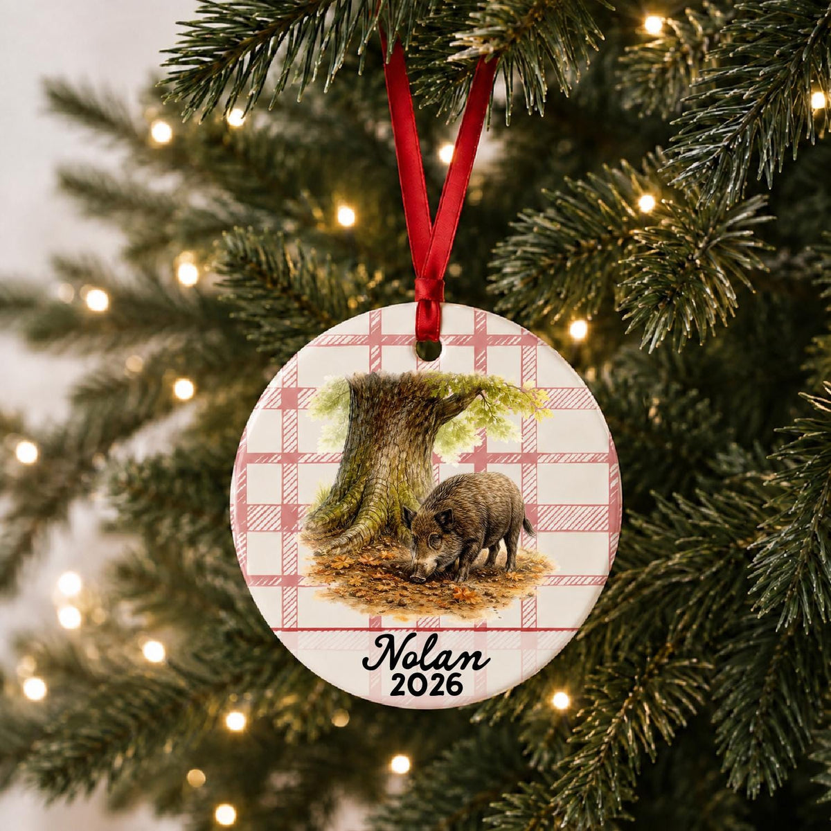 Personalized wild boar ceramic ornament with name and year on red plaid hanging on a lit Christmas tree