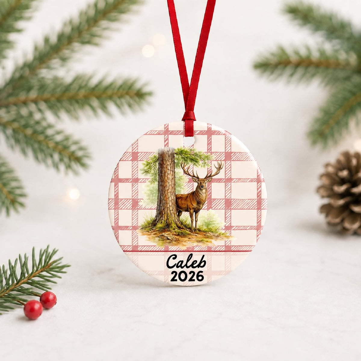Personalized red deer stag ceramic ornament with name and year on red plaid with red ribbon on a white surface with pine branches and pinecones