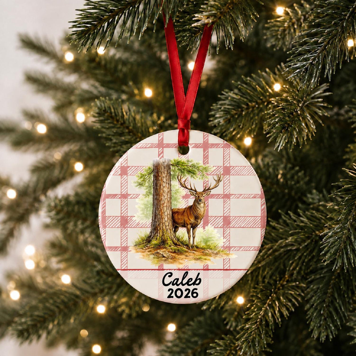 Personalized red deer stag ceramic ornament with name and year on red plaid hanging on a lit Christmas tree