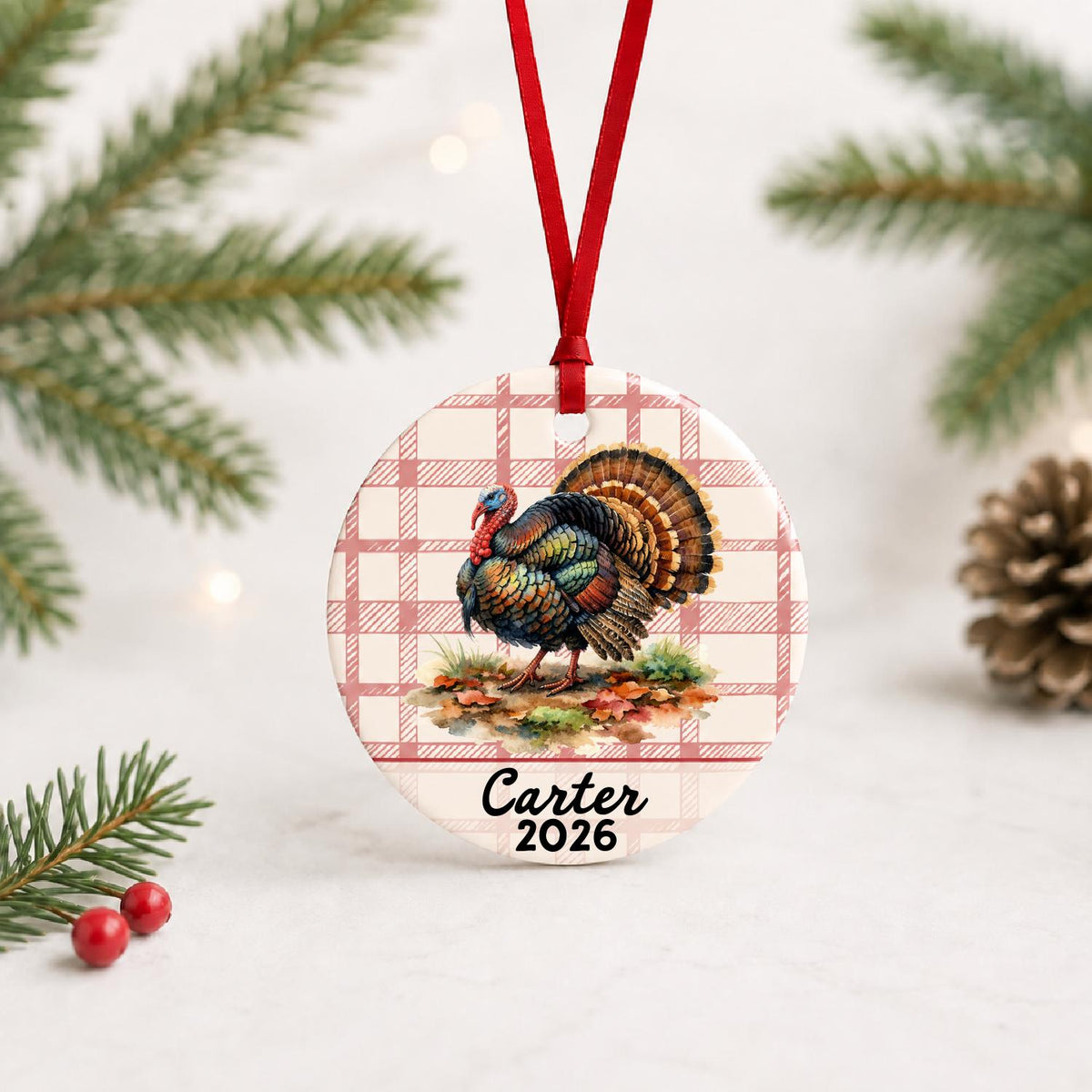 Personalized wild turkey ceramic ornament with name and year on red plaid with red ribbon on a white surface with pine branches and pinecones
