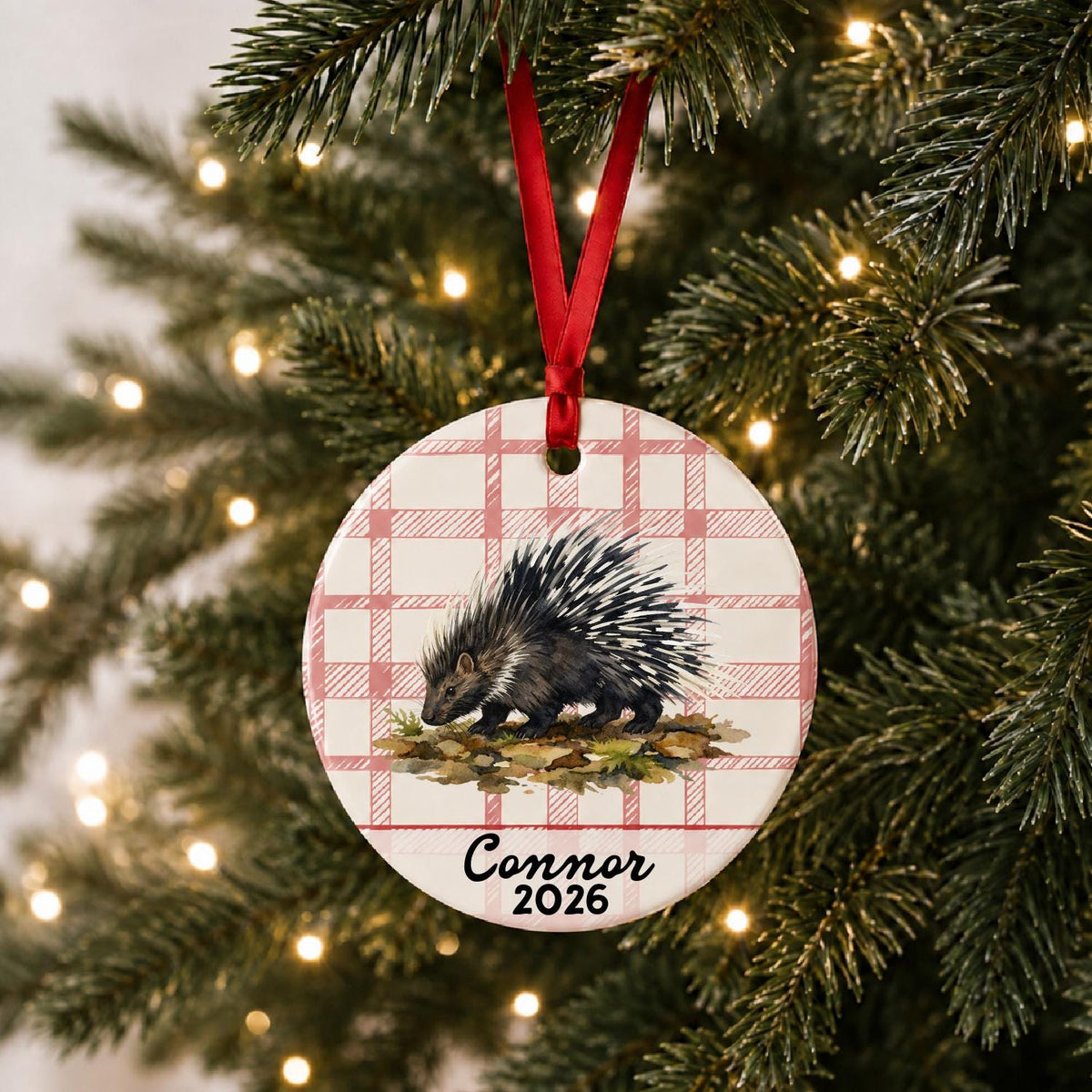 Personalized porcupine ceramic ornament with name and year on red plaid hanging on a lit Christmas tree