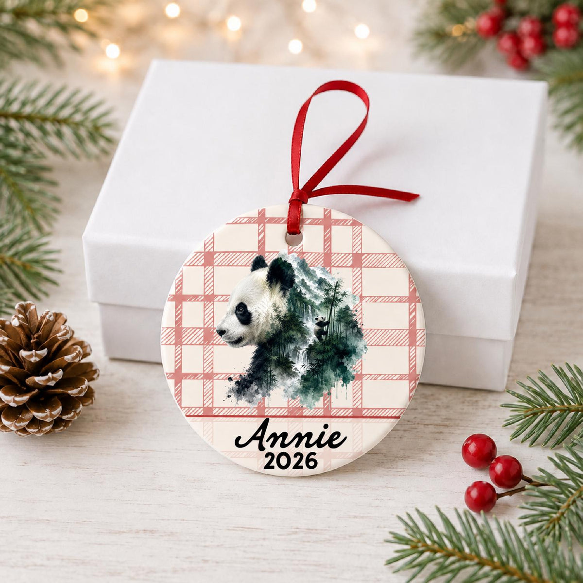 Personalized giant panda ceramic ornament with name and year on red plaid in front of a white gift box with pinecones and red berries