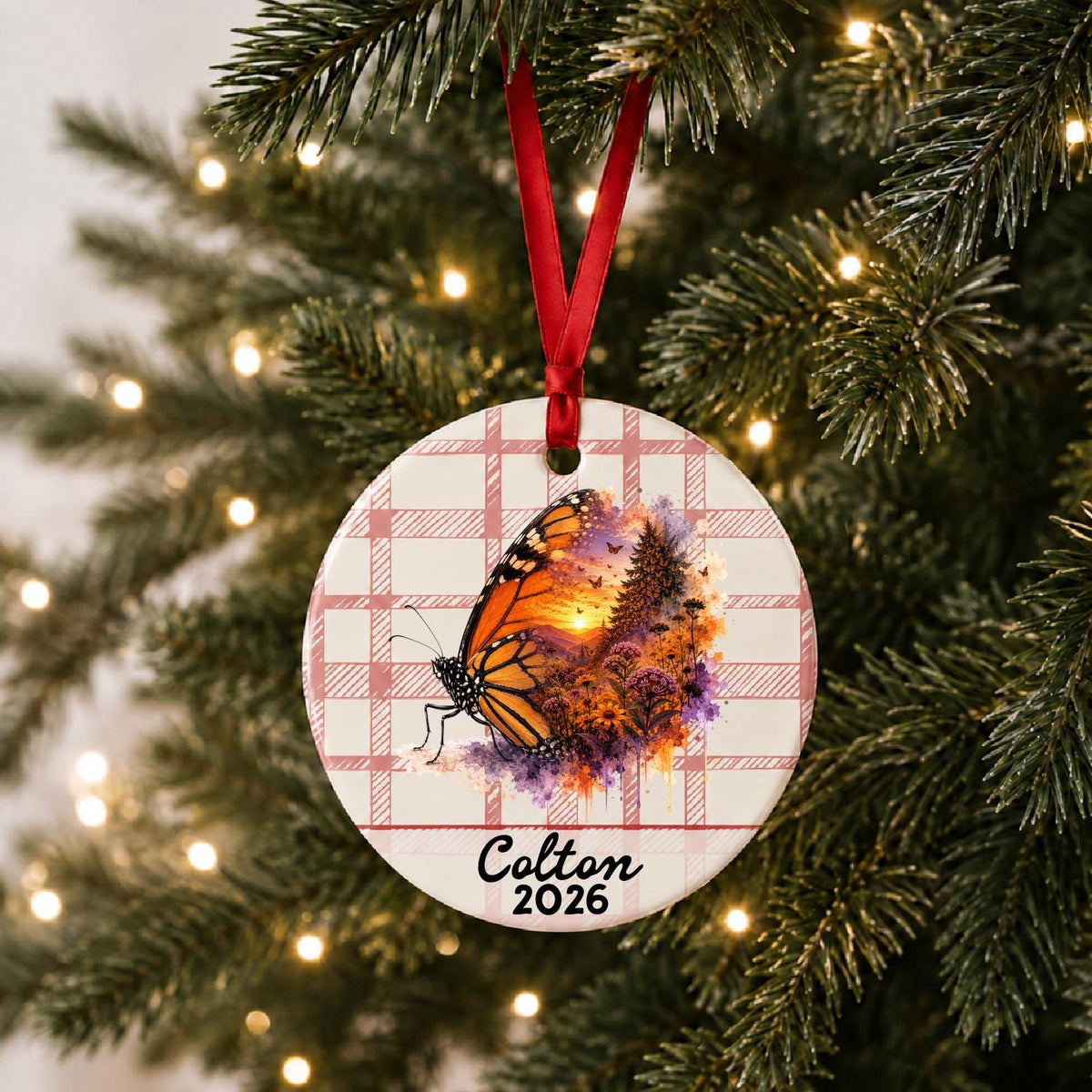 Personalized monarch butterfly ceramic ornament with name and year on red plaid hanging on a lit Christmas tree