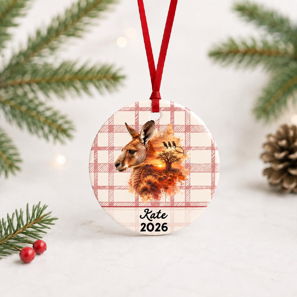Personalized red kangaroo ceramic ornament with name and year on red plaid with red ribbon on a white surface with pine branches and pinecones