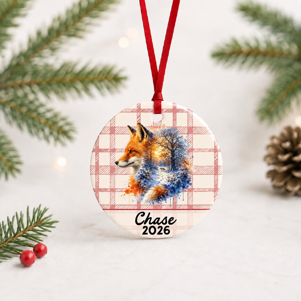 Personalized red fox ceramic ornament with name and year on red plaid with red ribbon on a white surface with pine branches and pinecones