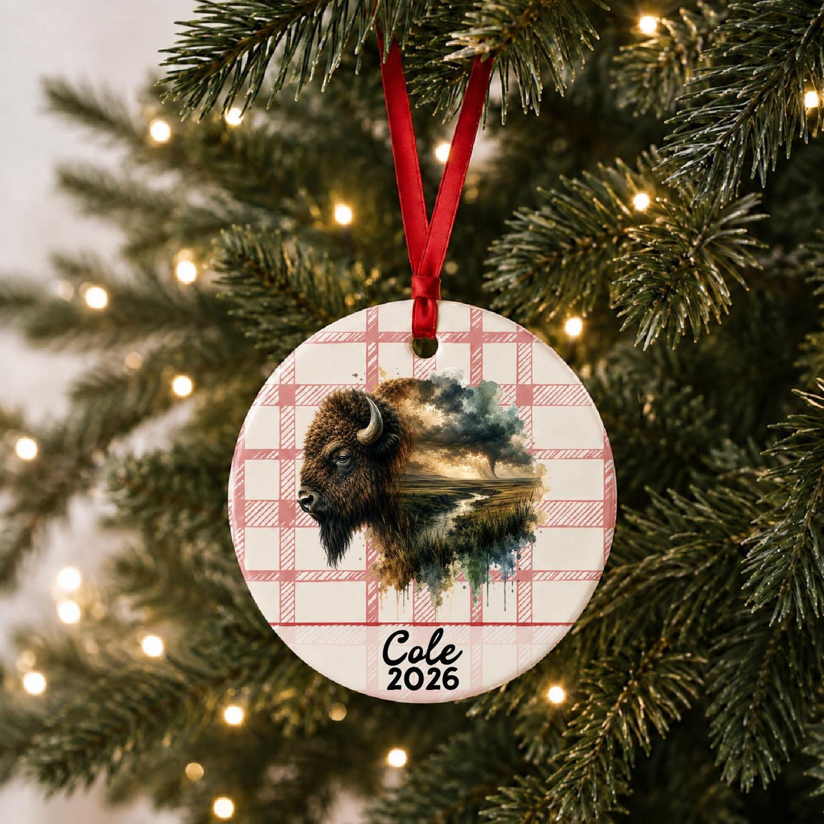 Personalized american bison ceramic ornament with name and year on red plaid hanging on a lit Christmas tree