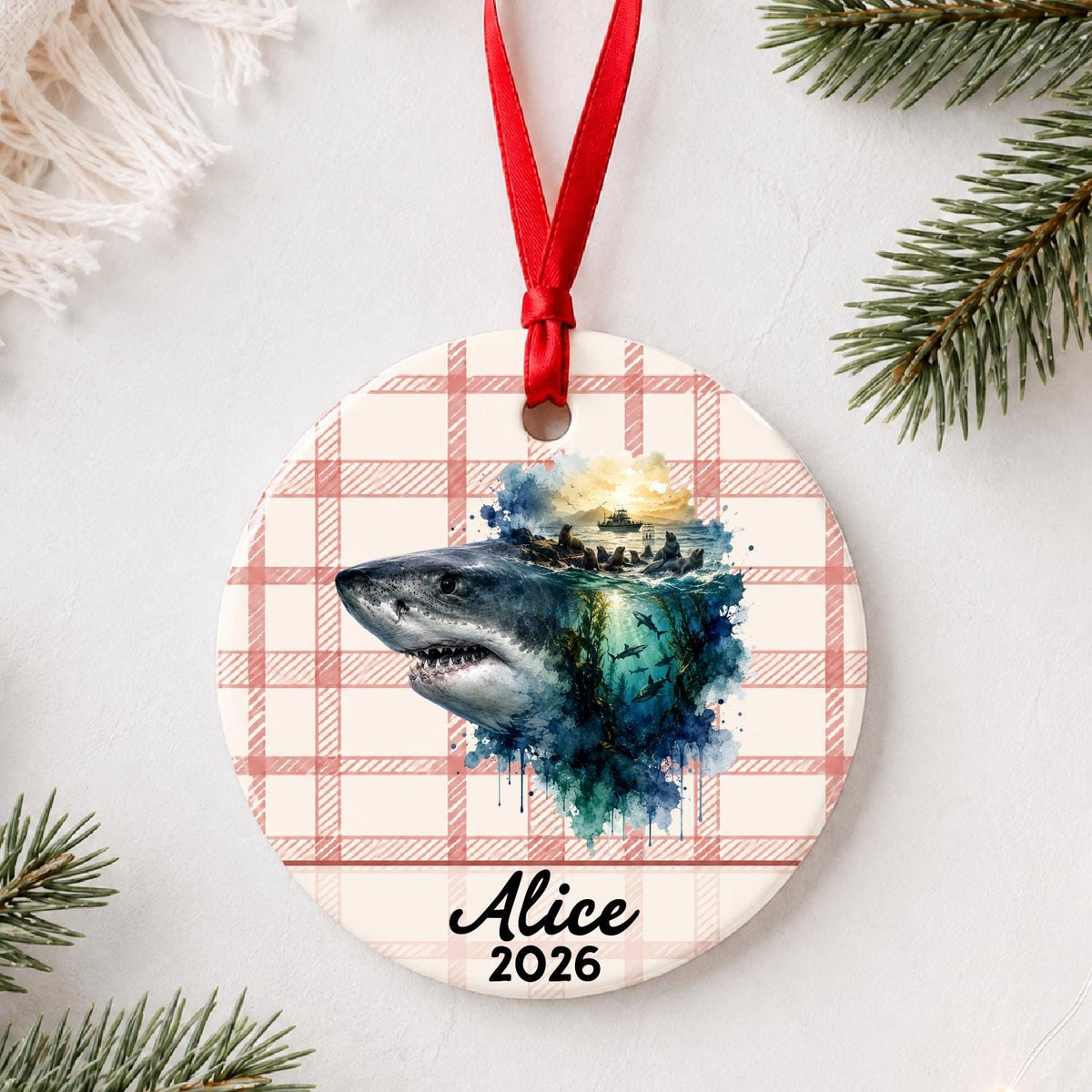 Personalized great white shark ceramic ornament with name and year on red plaid styled with pine branches on a soft white background