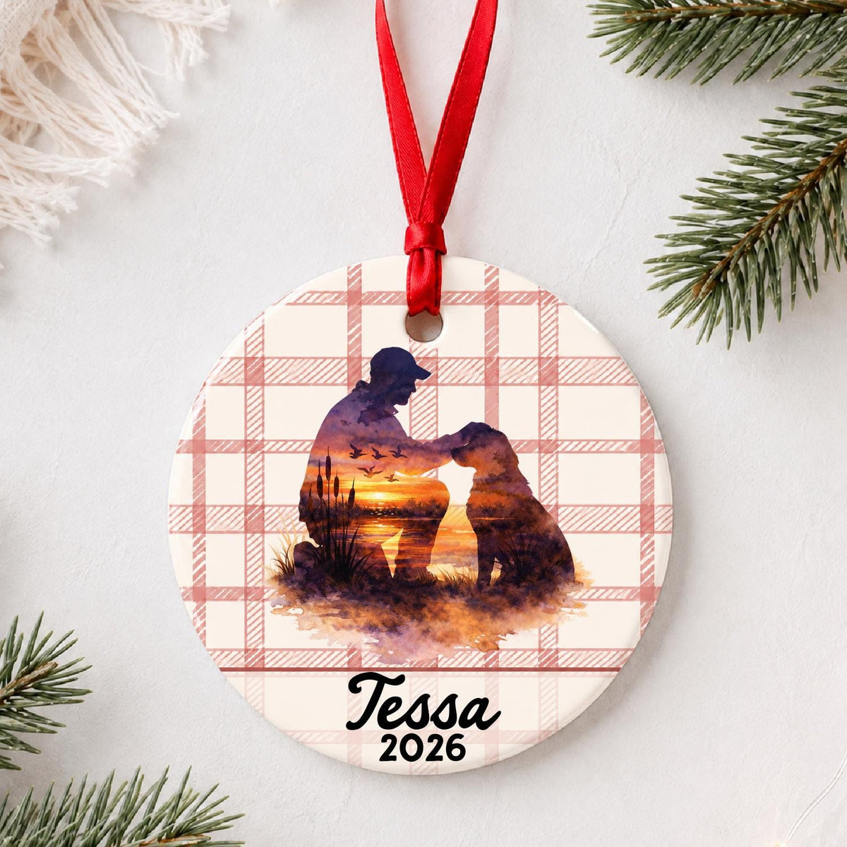 Personalized hunter and dog ceramic ornament with name and year on red plaid styled with pine branches on a soft white background