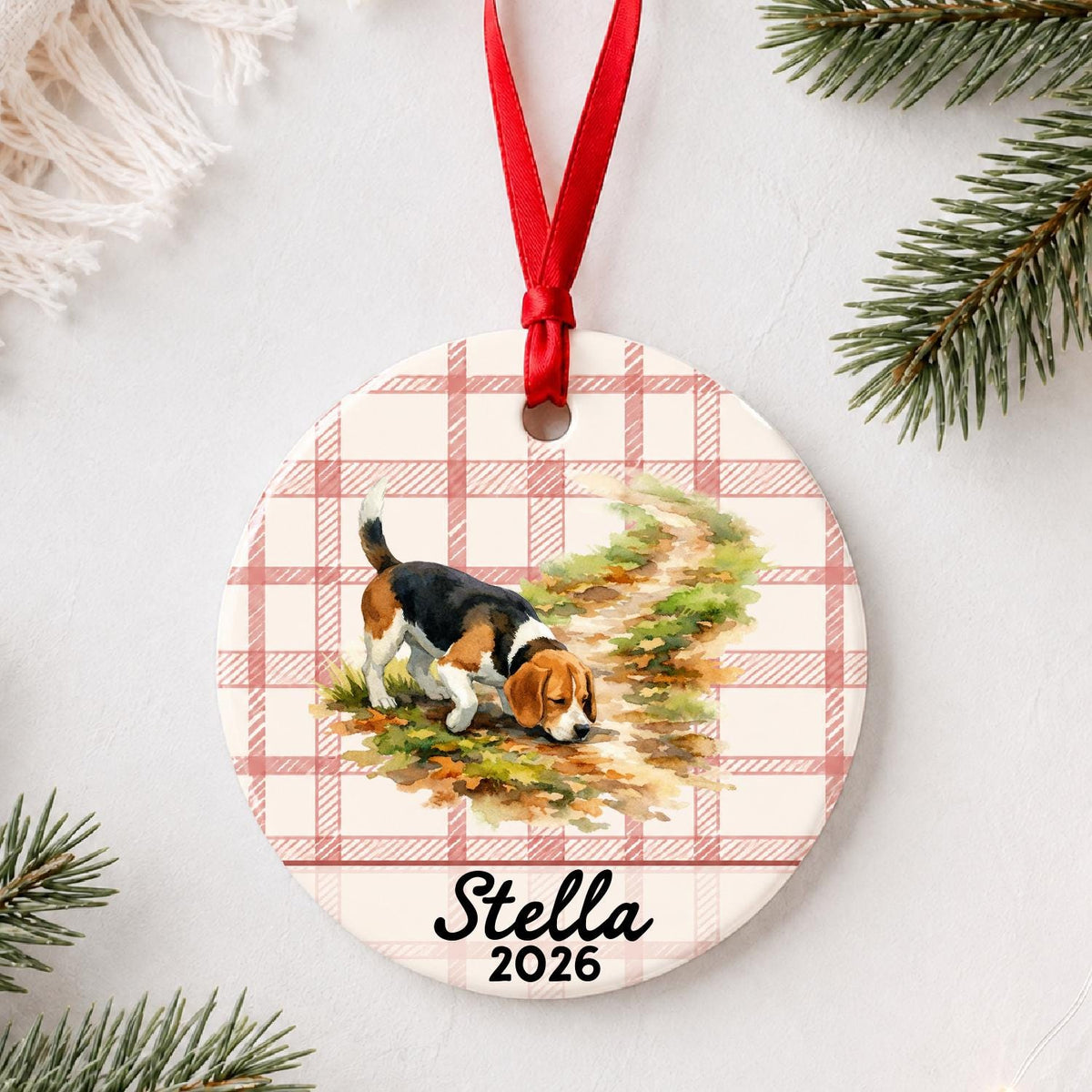 Personalized beagle ceramic ornament with name and year on red plaid styled with pine branches on a soft white background