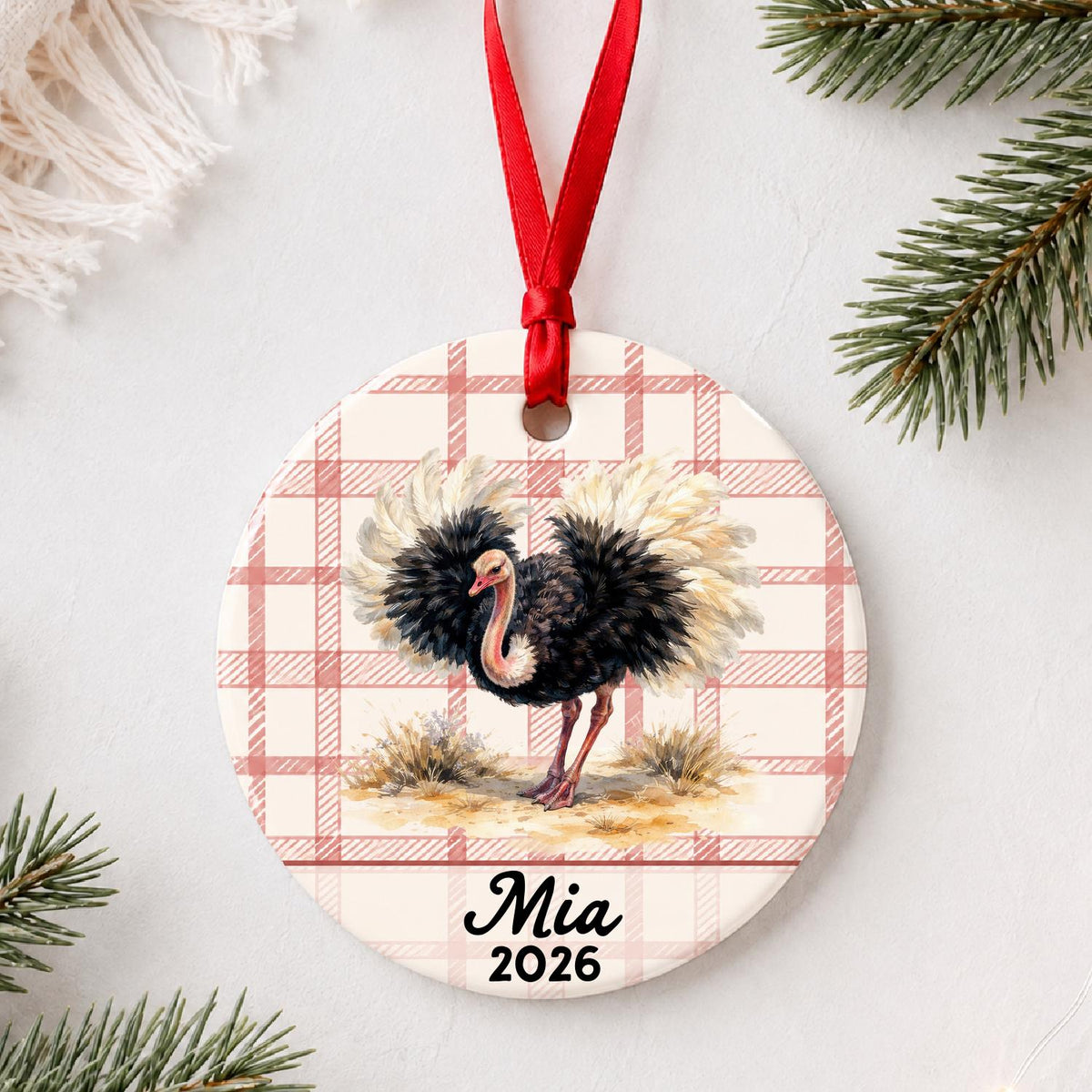 Personalized ostrich ceramic ornament with name and year on red plaid styled with pine branches on a soft white background