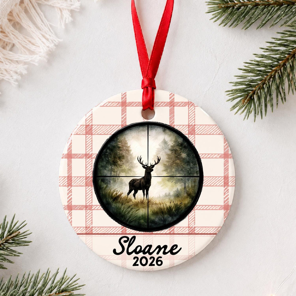 Personalized deer hunting ceramic ornament with name and year on red plaid styled with pine branches on a soft white background