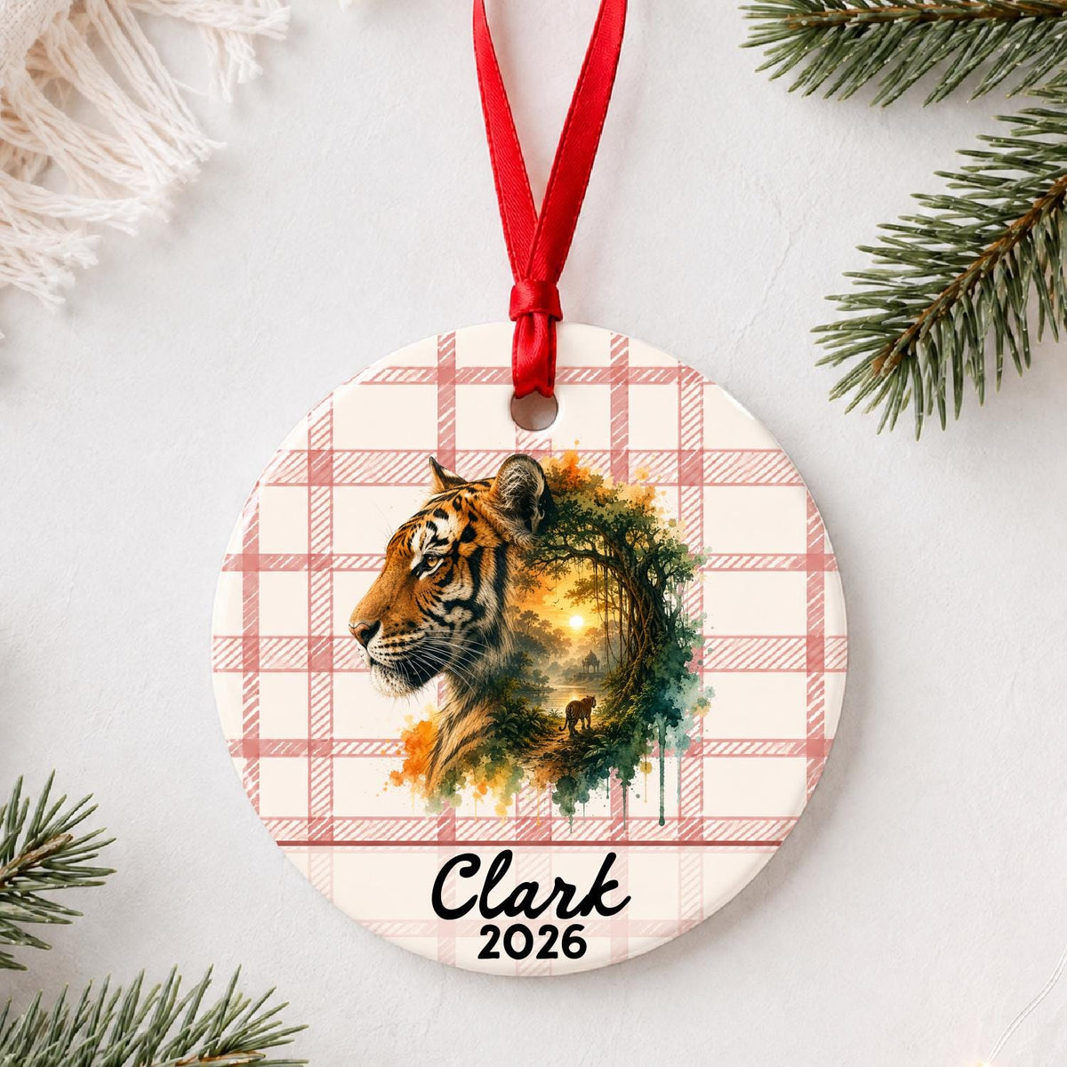 Personalized tiger ceramic ornament with name and year on red plaid styled with pine branches on a soft white background