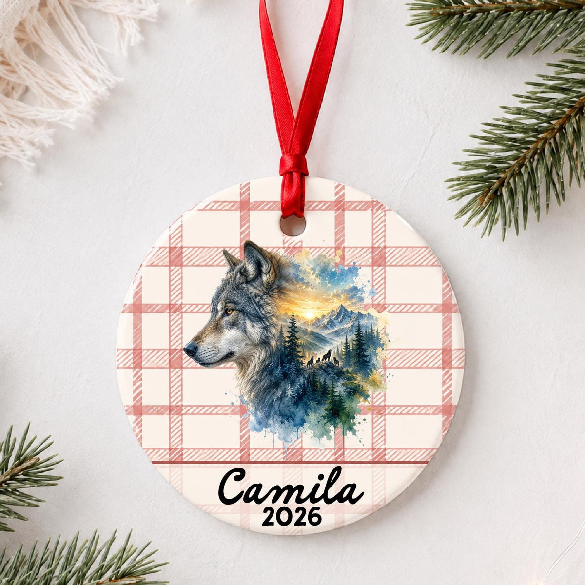 Personalized grey wolf ceramic ornament with name and year on red plaid styled with pine branches on a soft white background