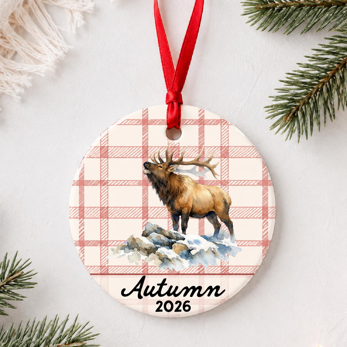 Personalized bull elk ceramic ornament with name and year on red plaid styled with pine branches on a soft white background