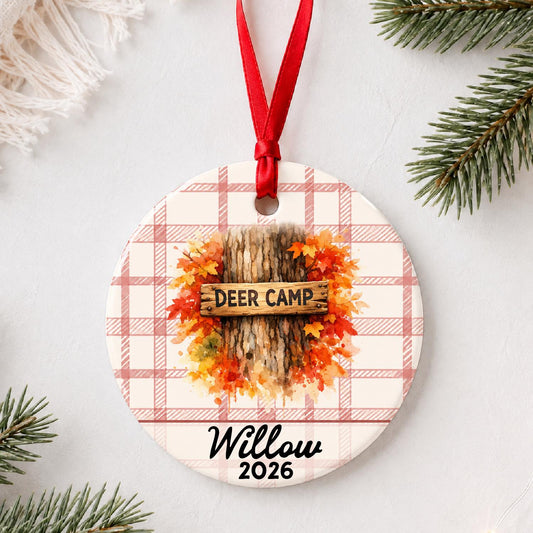 Personalized deer camp ceramic ornament with name and year on red plaid styled with pine branches on a soft white background