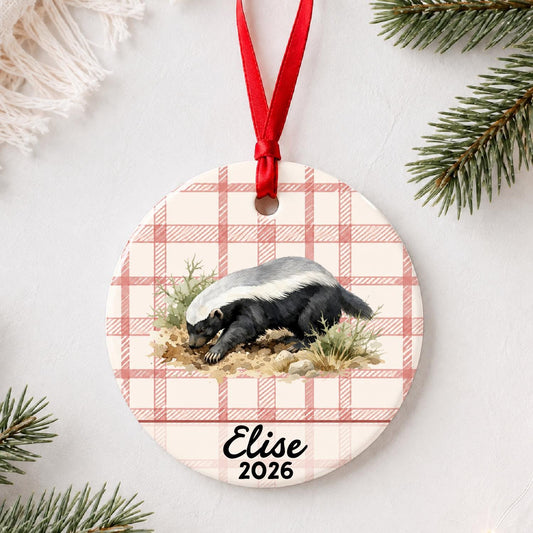 Personalized honey badger ceramic ornament with name and year on red plaid styled with pine branches on a soft white background