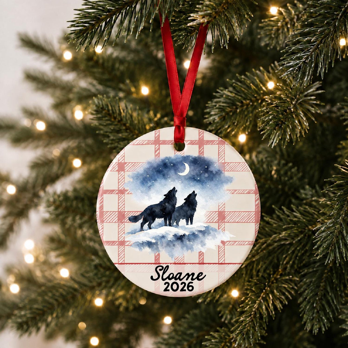 Personalized howling wolf pair ceramic ornament with name and year on red plaid hanging on a lit Christmas tree