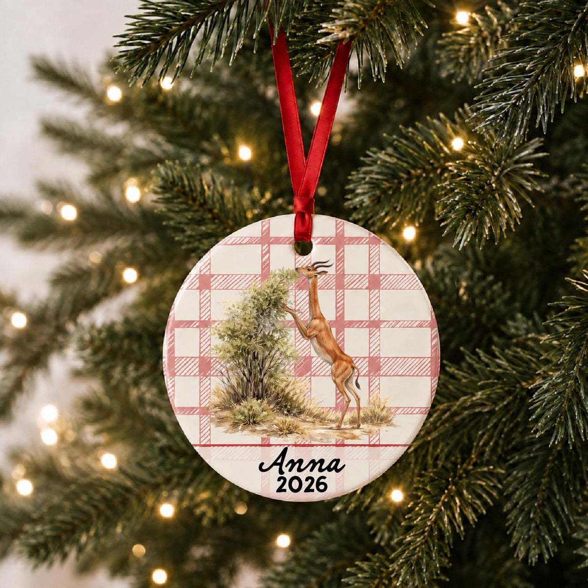 Personalized gerenuk ceramic ornament with name and year on red plaid hanging on a lit Christmas tree
