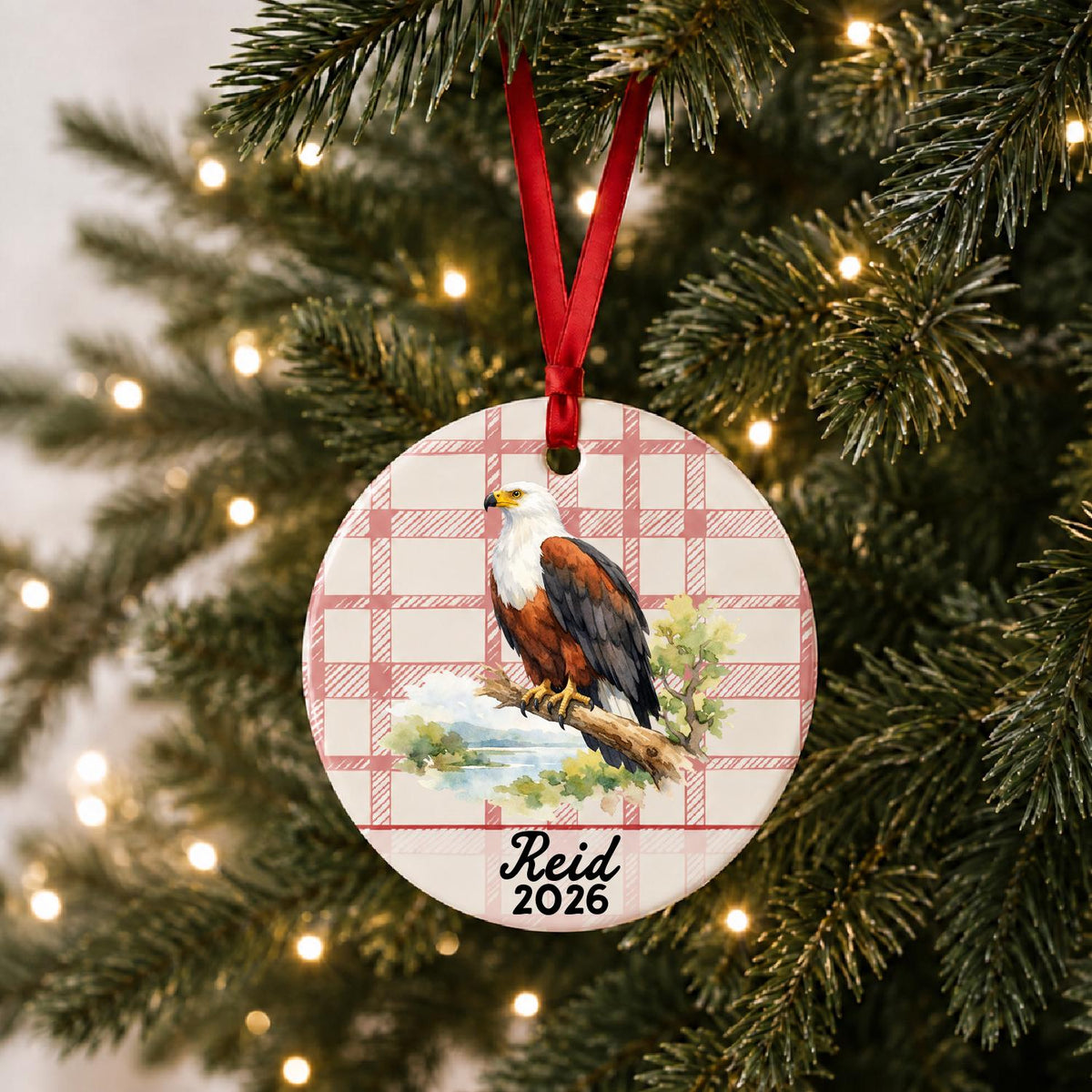 Personalized african fish eagle ceramic ornament with name and year on red plaid hanging on a lit Christmas tree