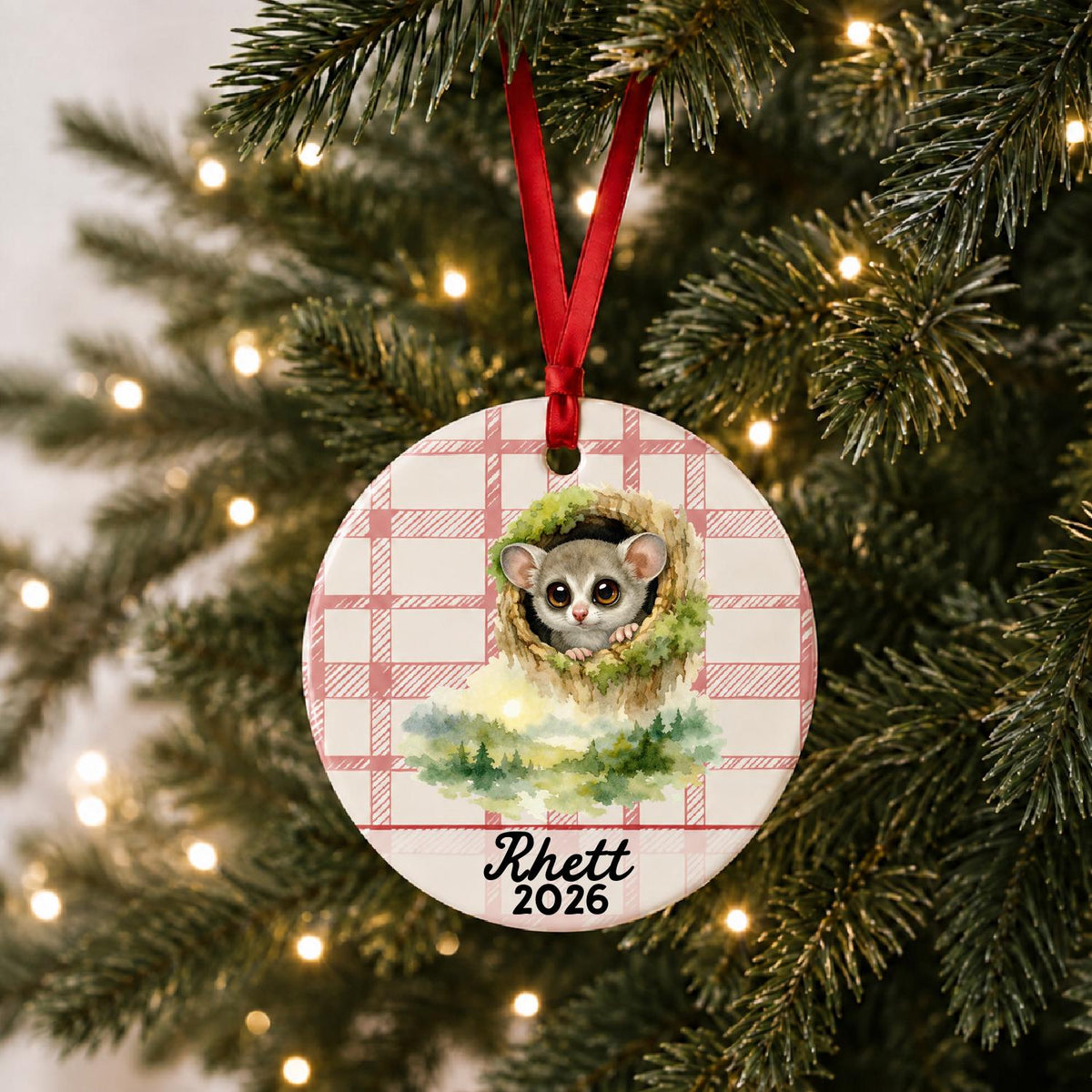 Personalized galago ceramic ornament with name and year on red plaid hanging on a lit Christmas tree